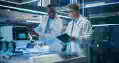 Portrait of Two Diverse Male Industrial Robotics Specialists Working on a Mobile Robot. Caucasian And Black Engineers In Lab Coats Discussing an Automated Robotic Delivery Assistant with AI.
