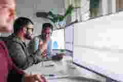 Three colleagues analyze data trends, working closely with monitors displaying dynamic charts and graphs in a modern tech office environment