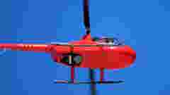 red helicopter flying in the blue sky. View from the ground, with highlights for the blades and landing gear