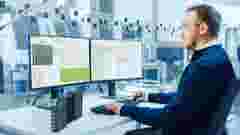 Engineer Working on a Computer, Two Monitor Screens Show BK Connect Software. Modern Factory with High-Tech Machinery.