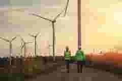 two engineers walking towards a windmill farm at sunset ready for inspection