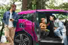 Road in woodland. Mother, father and little son are waiting for electric car to charge outdoors.