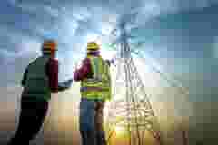Two electrical engineers with notebooks stand in front of a high voltage pole