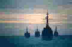 Four frigates exercising on the ocean at sunset.
