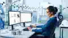 Female Industrial Engineer Solving Problems, Working on a Personal Computer, Two Monitor Screens Show CAD Software with 3D Prototype of Zero-Emissions Engine Being Tested. Working Modern Factory
