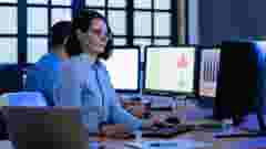 Two professional engineers are deeply engrossed in analyzing complex data on multiple monitors in a late-night office setting